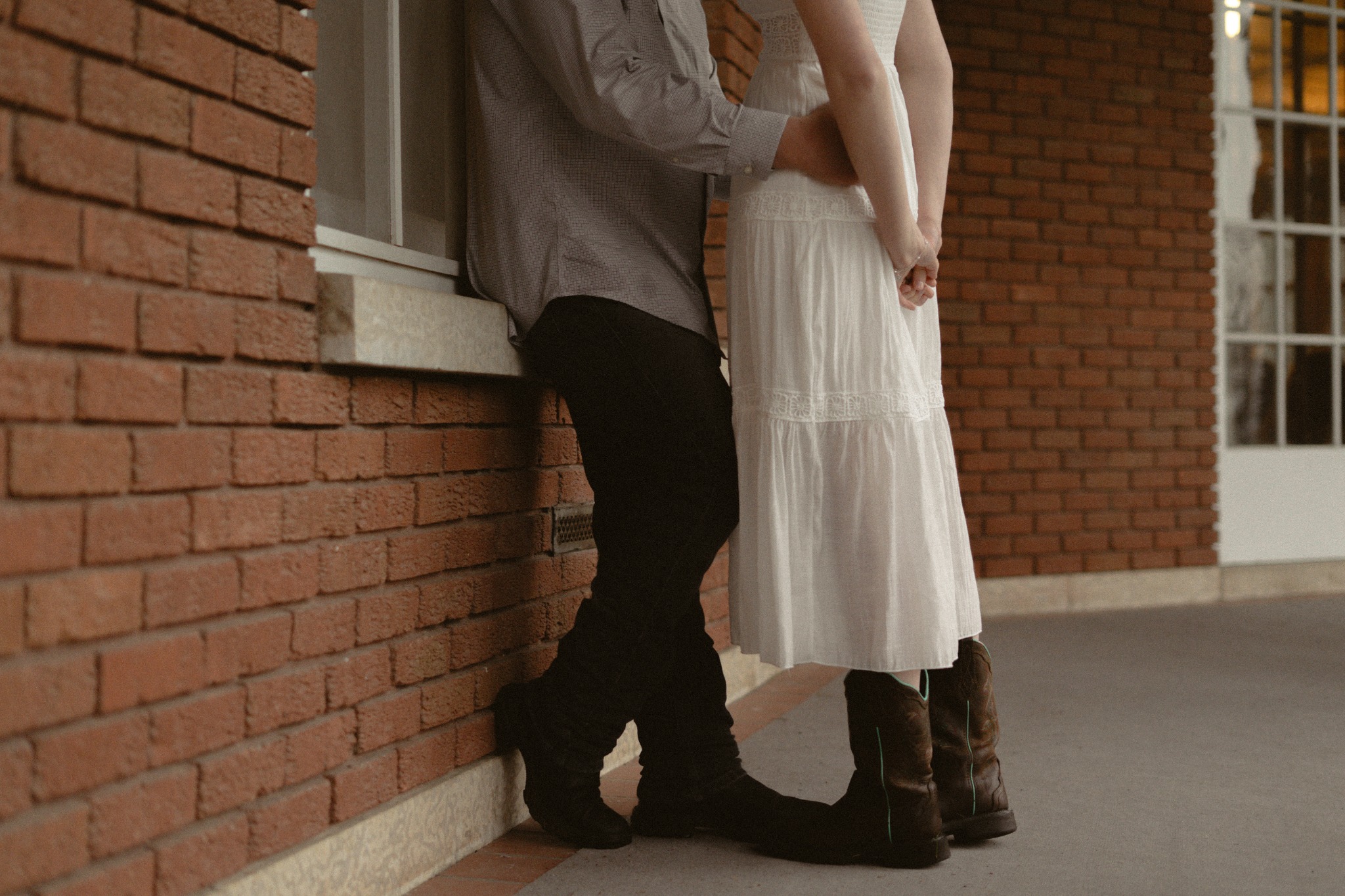 An engaged couple standing close beside a brick wall
