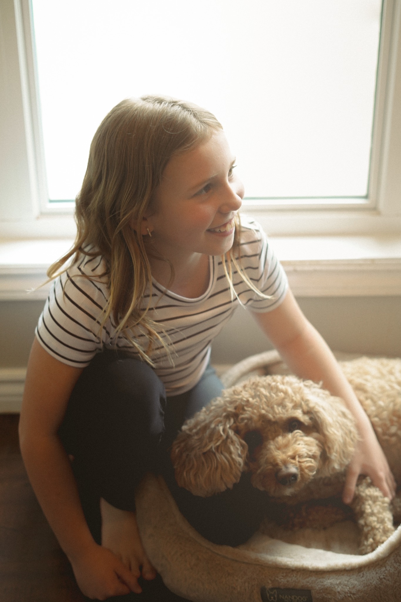 A girl sitting with her dog beside a bright window