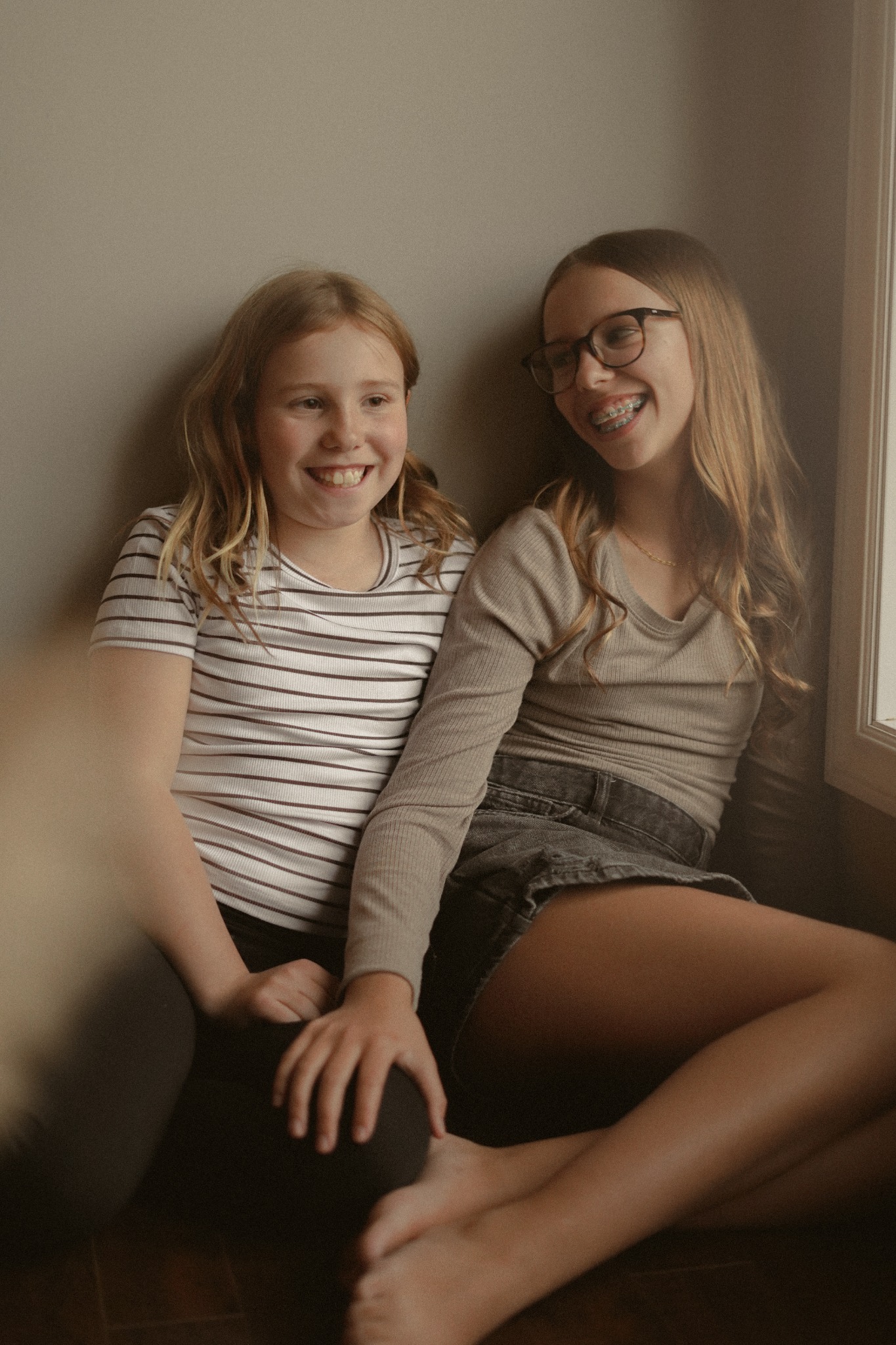 Two sisters sitting together beside a window